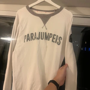Vit långärmad tröja Parajumpers - Vit långärmad tröja från Parajumpers med grå detaljer vid halsringningen och tryckt logga på bröstet. Tröjan har en klassisk passform och patch på ena ärmen. Perfekt för dig som gillar stilrena och sportiga plagg.