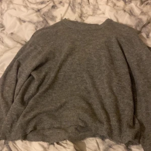 Grå stickad tröja med rund hals - Mysig grå stickad tröja med rund hals och avslappnad passform. Perfekt för kyliga dagar och enkel att matcha med jeans eller kjol. Tröjan har långa ärmar och är superbekväm att bära.