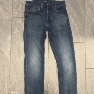 Blå jeans från Jack & Jones, stl 28/30 - Säljer ett par klassiska blå jeans från Jack & Jones i storlek 28/30. Modellen är slim/glenn. Jeansen har en snygg tvätt med lätt slitning och raka ben. Tillverkade i mjukt jeanstyg som är sköna att bära hela dagen. Perfekta för dig som gillar en enkel och stilren look.