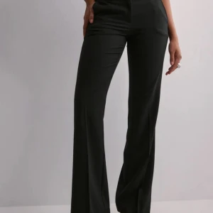 Svarta vida kostymbyxor - Snygga svarta kostymbyxor med hög midja och vida ben. Byxorna har en klassisk look och är tillverkade i ett mjukt material som ger en skön passform. Perfekta för dig som gillar stilrena och trendiga plagg.