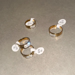Guldiga ringar med glittriga stenar - Säljer flera snygga guldiga ringar med glittriga stenar framtill. Ringen har en klassisk rund form och är dekorerad med små, skimrande stenar som ger extra bling. Perfekt för dig som vill ha något som sticker ut och glänser.