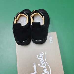 Svarta sneakers från Christian Louboutin - Snygga svarta sneakers från Christian Louboutin i mocka med klassisk låg siluett. Skorna har svarta sulor och beige innersida som ger en lyxig känsla. Perfekta för dig som vill ha en stilren och exklusiv look.