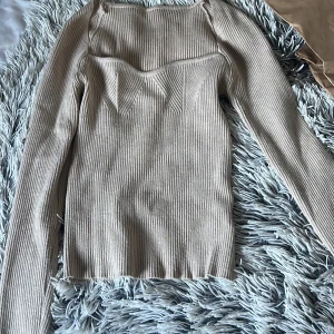 Beige ribbad långärmad tröja - Säljer en beige ribbad långärmad tröja med markerad byst och fyrkantig halsringning. Tröjan har en figurnära passform och är perfekt för dig som gillar stilrena och trendiga plagg. Superenkel att matcha med både jeans och kjol.