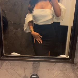 Svart och vit långklänning med slits - Säljer en elegant långklänning i svart och vitt med offshoulder och puffiga ärmar. Klänningen har en figurnära passform och en hög slits framtill som ger en snygg touch. Perfekt för dig som vill sticka ut med stilrena detaljer och trendig design.