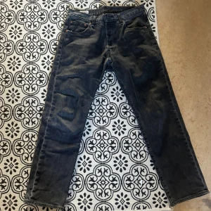 Levi's 501 grå jeans straight fit - Grå Levi's 501 jeans med klassisk straight fit och fem fickor. Jeansen har en snygg vintage-vibe med den ikoniska läderpatchen bak och röd Levi's-tag på fickan. Tillverkade i slitstarkt denim med knappgylf och normal passform.