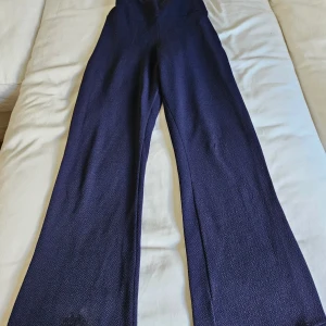 Mörkblå vida byxor med struktur - Snygga mörkblå byxor med vid passform och hög midja. Materialet har en cool, strukturerad yta som ger en extra touch. Perfekt om du gillar en lite lösare och trendig look. De har ett brännmärke i järn längst ner på ena benet (se sista bilden). Men det är inte särskilt tydligt när man har dem på sig.