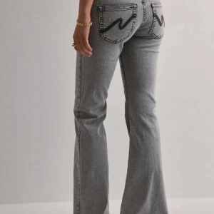 Grå bootcut jeans från Nelly - Snygga grå jeans från Nelly med bootcut passform och klassisk femficksdesign. Baktill finns tydliga svarta zigzag-broderier på fickorna som ger en cool detalj. Jeansen har hög midja och är tillverkade i mjukt jeanstyg med kontrastsömmar.helt nya ,säljs pågrund av att de inte passar mig 