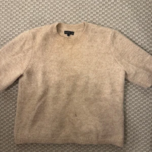 Beige stickad tröja från STOCKH LM - Mysig beige stickad tröja från STOCKH LM i storlek S. Tröjan har rund hals och korta ärmar, perfekt för lager-på-lager. Materialet är mjukt och fluffigt, vilket gör den extra skön att bära. Enkel och stilren design som funkar till många olika looks.
