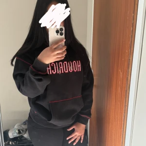 Svart HOODRICH hoodie med röd detalj - Svart hoodie från HOODRICH med röd kontrastsöm och broderad logga framtill. Texten 'From Nothing to Something' är broderad på ryggen och huvan.