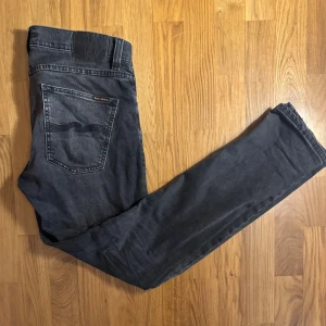 Nudie Jeans - Snygga svarta jeans från Nudie Jeans med klassisk femficksdesign och diskret vågdetalj på bakfickorna. Jeansen har en rak passform och är tillverkade i mjukt denimtyg. Perfekta för dig som gillar en stilren look med mörk tvätt. Ny Pris 1699.