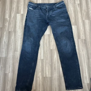Mörkgrå/svarta jeans från Diesel - Säljer ett par mörkblå jeans från Diesel med klassisk femficksdesign och snygg tvätt. Jeansen har raka ben och normal passform, tillverkade i bomull. Bakfickan har den typiska Diesel-detaljen och patchen i midjan ger extra edge.