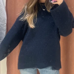 Mörkblå stickad tröja i loose fit - Mysig Ginatricot mörkblå stickad tröja med loose passform och långa breda ärmar. Perfekt för kyliga dagar och enkel att styla med jeans eller kjol. Tröjan har en klassisk rund halsringning och är superbekväm att bära, från deras premium collection i ull!