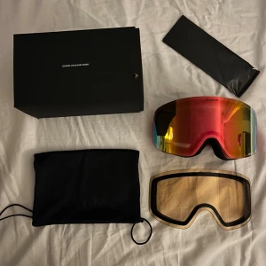 Chimi skidglasögon med extra lins - Säljer ett par Chimi skidglasögon med spegelröd lins och rosa band. Medföljer extra gul lins, förvaringspåse och originalbox. Snygg och modern look, perfekt för dig som vill sticka ut i backen.