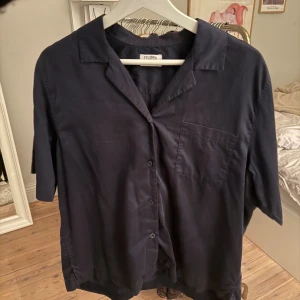 Mörkblå skjorta från Filippa K - Stilren unik mörkblå skjorta från Filippa K med kort ärm, klassisk krage och bröstficka. Skjortan har knäppning framtill och är tillverkad i ett mjukt, svalt material som ger en avslappnad känsla. Perfekt till kontoret eller middagar för en stilren look🥰Från säsong 2025, nypris: 1900 kr💞Går inte att köpa längre, i jättebra skick. Skriv för fler bilder🤍🤍