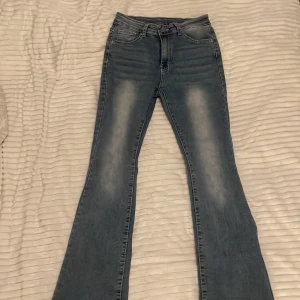 Blå bootcut jeans med detaljer - Snygga ljusblå bootcut jeans med coola detaljer på bakfickorna. Klassisk femficksmodell med knapp och dragkedja. Jeansen har en hög midja och är tillverkade i stretchigt denim för skön passform (Uppsydda). Mått: Min längd 161cm, innerbenslängd på byxorna 71cm. Storlek på byxorna: 40-42.                                                                Jeansen är använda och har små defekter, vilket kan ses vid noga inspektion. 
