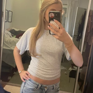 Grå croppad t-shirt från 157 - En enkel och stilren ljusgrå croppad t-shirt från 157. Modellen har korta ärmar och rund halsringning. Perfekt till jeans eller shorts för en avslappnad look.🥰