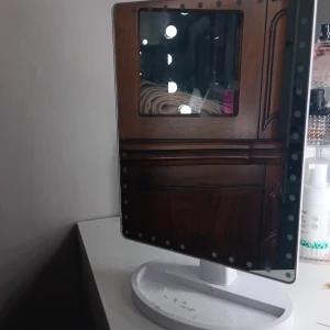 LED Sminkspegel med touch - Modern sminkspegel med inbyggda LED-lampor runt kanten för optimal belysning. Touch-funktion för att justera ljusstyrkan. Står stadigt på en vit fot med förvaringsyta, dock syns viss smuts/slitage på foten. Perfekt för makeup och styling.