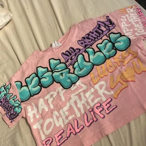 Rosa crop top med graffiti från Zara - Cool rosa crop top från Zara med färgglada graffiti-prints i turkos, lila, vit, gul och rosa. T-shirten har korta ärmar och är tillverkad i mjuk bomull. Perfekt för dig som gillar streetstyle och unika tryck!