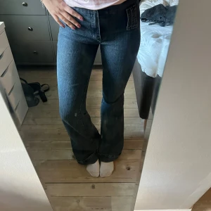 bootcut jeans med hög midja - Mörkblå jeans köpta på secondhand i Amsterdam med bootcut passform och hög midja. Klassisk denim med snygga detaljer utan fickor men sitter snyggt. Jeansen är bootcut och har stretch. Sitter jättebra på mig som är 170 cm lång. Skulle säga storlek 38. Vet inte märket men de är bra kvalitet.