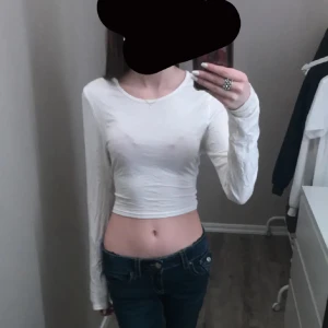 Vit croppad långärmad topp med snörning - Säljer en vit, croppad långärmad topp med snygg snörning i ryggen. Tunn och mjuk i materialet, perfekt för dig som gillar en enkel men trendig look. Rund halsringning och figurnära passform som framhäver midjan.