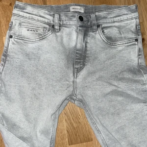 Grå jeans från GANT med straight fit - Snygga ljusgrå jeans från GANT med klassisk femficksdesign och logga på myntfickan. Jeansen har rak passform, bälteshällor och knappstängning fram. Materialet är jeans med en tvättad look som ger en cool vibe.