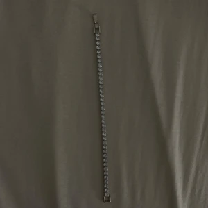 Silverfärgat armband med stenar - Ett smalt och elegant armband i silverfärg med en rad gnistrande stenar längs hela bandet. Klassisk design med fyrkantiga länkar på baksidan och säker låsning. Perfekt för dig som gillar stilrena smycken med lite extra bling.