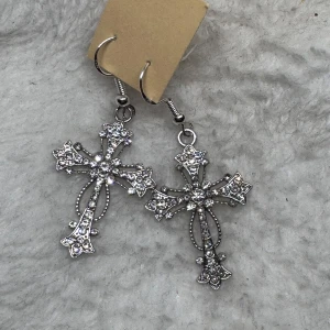 Glittriga korsörhängen i silver - Snygga örhängen i form av kors med glittrande stenar. De är silvriga och har detaljerade mönster som ger en cool och unik look. Perfekta för dig som vill sticka ut med accessoarer som syns. Tips till julkalendern 