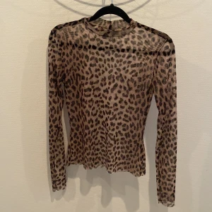 Leopardmönstrad mesh-top från Gina Tricot - Säljer en transparent långärmad topp från Gina Tricot i leopardmönster. Toppen är i tunn mesh med beige och bruna toner, har en tight passform och hög hals. Perfekt att styla med jeans eller kjol för en cool look. Jättefin med en väst över!
