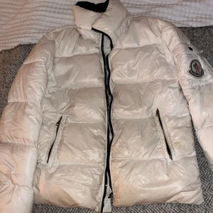 Vit Moncler pufferjacka med logga - Intressekoll!! Snygg vit herrjacka från moncler, min killes gammla som aldrig kommer till användning längre! Det står ingen storlek på jackan men han har för det mesta storlek M, så skulle gissa på att även jackan är drtsamma. Skicket är bra men har lite smutsfläckar här och där, vet ej om det är något som kan tvättas bort.