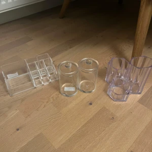 Genomskinliga sminkförvaringar - Säljer ett set med tre olika sminkförvaringar i transparent akryl och glas. En rektangulär organiserare med flera fack, två runda glasburkar med lock och en lila akrylbehållare med tre fack i olika höjder. Perfekt för sminkborstar, läppstift och småprylar. Kan köpa de separat och då bara kontakta mig så diskuterar vi priset