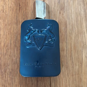 Parfums de Marly Layton EdP 125ml - Säljer en Parfums de Marly Layton Eau de Parfum, 125ml. Flaskan är matt mörkblå med silverfärgat lock och har ett stilrent reliefmönster med två hästar och sköld. Medföljer originalkartong i svart med vita ränder och silverdetaljer.