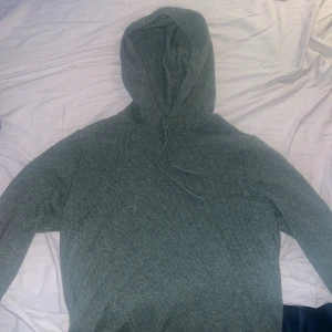 Grå stickad hoodie med huva - Mysig grå stickad hoodie med huva och snörning. Tröjan har lång ärm och är ribbstickad för extra komfort. Perfekt för dig som gillar en chill och enkel stil. Passar lika bra till jeans som till mjukisbyxor.