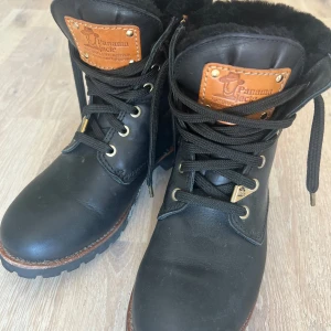 Svarta boots från Panama Jack - Säljer ett par svarta boots från Panama Jack med grov sula och snörning. Skorna är fodrade med mjuk svart päls och har detaljer i brunt skinn vid plösen. Perfekta för kalla dagar och har en rund tå samt robust design.