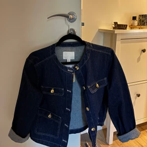Mörkblå jeansjacka med guldknappar - Snygg mörk blå jacka helt ny ,och kan både klä upp eller en mer avslappnad look. Perfekt för dig som gillar klassisk denimstil (.Ny pris 599)
