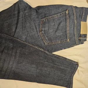 Blå jeans från Zara, storlek 42/32 - Snygga klassiska blå jeans från Zara med fem fickor och kontrastsömmar. Jeansen har rak passform och normal midja, tillverkade i slitstarkt denimtyg. Perfekta till en avslappnad stil och funkar året runt.