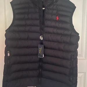 mörkblå dunväst från Polo Ralph Lauren - mörkblå dunväst från Polo Ralph Lauren. Säljer pga ändrat mig och ska köpa ny väst. Helt ny. Står S i storlek men är som M