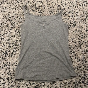 Supersöt linne från Schiesser - Grå linnetopp från Schiesser i mjuk bomullsmix. Toppen har smala axelband, v-ringning och två små knappar framtill. Enkel och stilren design som passar perfekt till jeans eller shorts.