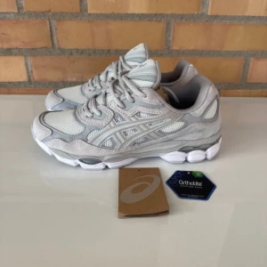 Gråvita Asics sneakers mesh & mocka - Snygga Asics sneakers i grått och vitt med coola detaljer. Ovandelen är i mesh och mocka för en sportig vibe och skön känsla. Sulan är rejäl och har Ortholite-dämpning för extra komfort. Perfekta för dig som gillar stilrena och fräscha sneakers.