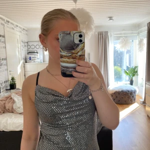 Glittrig silvertopp Sisters Point - Säljer en glittrig silverfärgad topp från Sisters Point i storlek S. Toppen har tunna axelband, omlottliknande drapering vid bysten och är täckt av små paljetter som ger en riktigt festlig vibe. Perfekt för dig som vill sticka ut och glänsa.