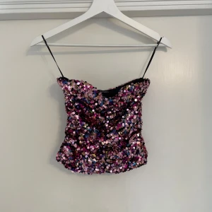 Glittrig paljettopp från Zara - Säljer en glittrig topp, täckt av rosa, lila och silvriga paljetter. Toppen har en snygg, figurnära passform som verkligen sticker ut. Perfekt för dig som vill glänsa extra mycket.
