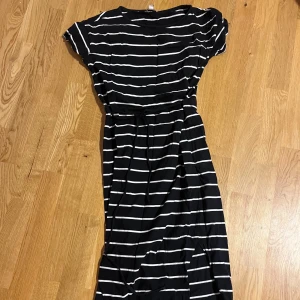 Knyt i midjan randig klänning från EDC - Svart klänning med vita horisontella ränder från EDC. Modellen har korta ärmar, rund hals och ett knytband i midjan för att skapa en snygg siluett. Mjuk och skön bomullskvalitet, perfekt för dig som gillar enkel och stilren design. NYTT SKICK