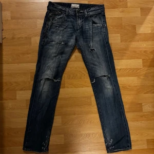 Jeans från Energie  - Säljer ett par mörkblå jeans med slitningar och hål på knäna för en cool, avslappnad look. Jeansen har raka ben, klassiska fem fickor och snygga detaljer på bakfickorna. Perfekta för dig som gillar streetstyle och vill ha ett par jeans med attityd.