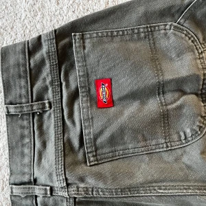 Mörkgröna cargopants från Dickies - Säljer ett par mörkgröna cargopants från Dickies med klassisk röd logga på bakfickan. Byxorna har raka ben, stora fickor på sidorna och är tillverkade i slitstark bomull. Perfekt för dig som gillar streetwear och funktionella detaljer.