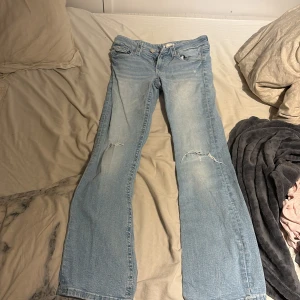 Ljusblå bootcut jeans från Gina Tricot - Säljer ett par ljusblå bootcut jeans från Gina Tricot i storlek 164. Jeansen har slitna detaljer på benen och klassisk femficksdesign. De är tillverkade i mjukt denimtyg och har en snygg, lite utsvängd passform nertill.