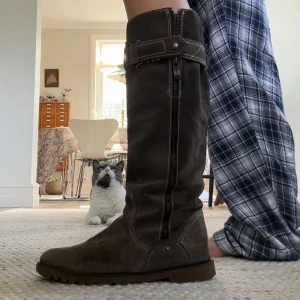 Bruna mockastövlar med spänne, strl 38 - Säljer mina älskade boots, då dom börjar bli försmå. Snygga knähöga stövlar i mörkbrun mocka med grov sula och dekorativt spänne upptill. Dragkedja på sidan och kontrastsömmar ger en cool look. Perfekta till höst- och vinteroutfits.
