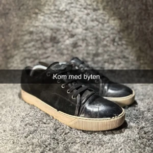 Svarta sneakers från Lanvin i mocka och lack - Svarta sneakers från Lanvin med ovandel i mocka och lackad tå. Klassisk modell med snörning och vit sula. Snygg kontrast mellan matta och blanka material ger en stilren vibe. Perfekta för dig som gillar exklusiva och tidlösa sneakers.