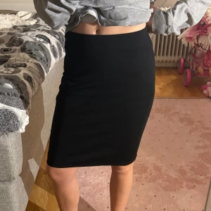 Svart tight kjol i bomull - Enkel och stilren svart kjol i tight passform. Kjolen är midjehög och slutar strax ovanför knäna, vilket ger en klassisk och clean look. Perfekt för dig som gillar minimalistisk stil och vill ha något som funkar till många olika outfits.