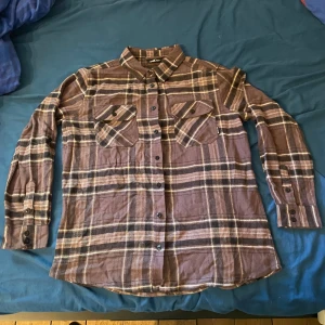 Rutig brun skjorta från Whistler - Säljer en snygg rutig skjorta från Whistler i bruna och beige toner. Skjortan har två bröstfickor med knappar, klassisk krage och långa ärmar. Tillverkad i mjuk bomull, perfekt för lager-på-lager-stil. Passar dig som gillar avslappnad och tidlös look.