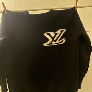 Svart stickad tröja Louis Vuitton - PRIS GÅR ATT DISKUTERA.                               Svart stickad tröja från Louis Vuitton med stor vit LV-logga på bröstet. Rund hals och långa ärmar, mjuk och skön känsla. Perfekt för dig som gillar exklusiva märken och vill ha en clean look med tydlig logga.
