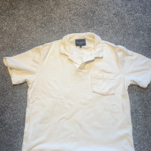 Vit frotté t-shirt från Bondelid - Fräsch vit t-shirt från Bondelid i mjuk frotté. Klassisk krage, korta ärmar och en bröstficka ger en chill och clean look. Perfekt för dig som gillar retrovibbar och vill ha något unikt i garderoben. Nypris 600